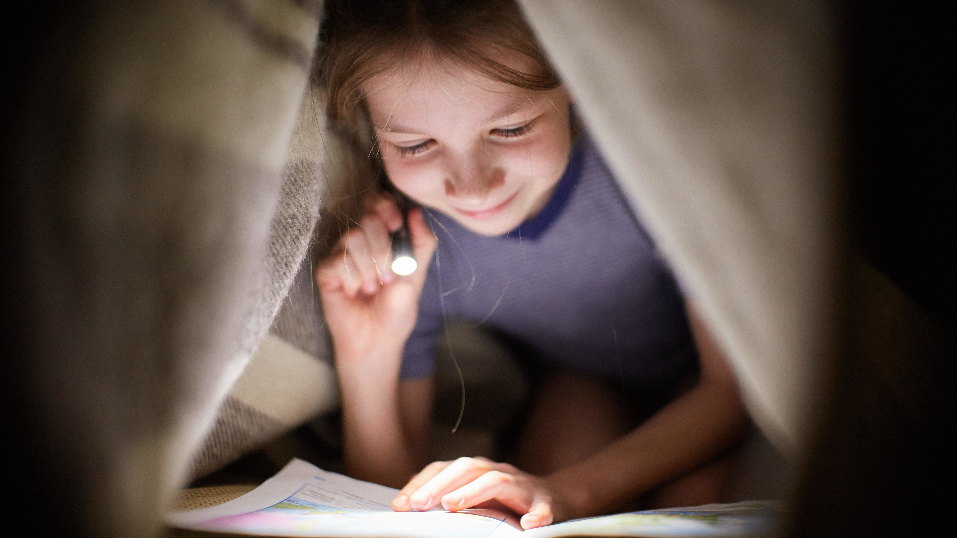 Girl reading under a blanket